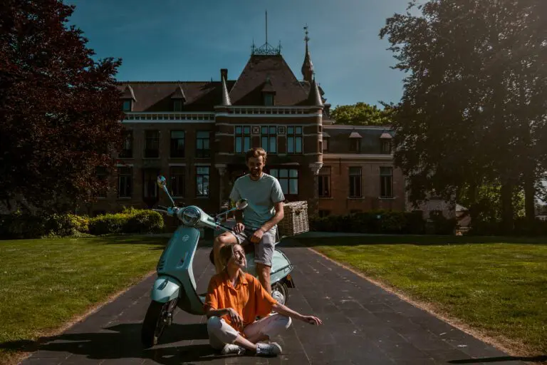 deux personnes assises avec une Vespa devant un beau bâtiment