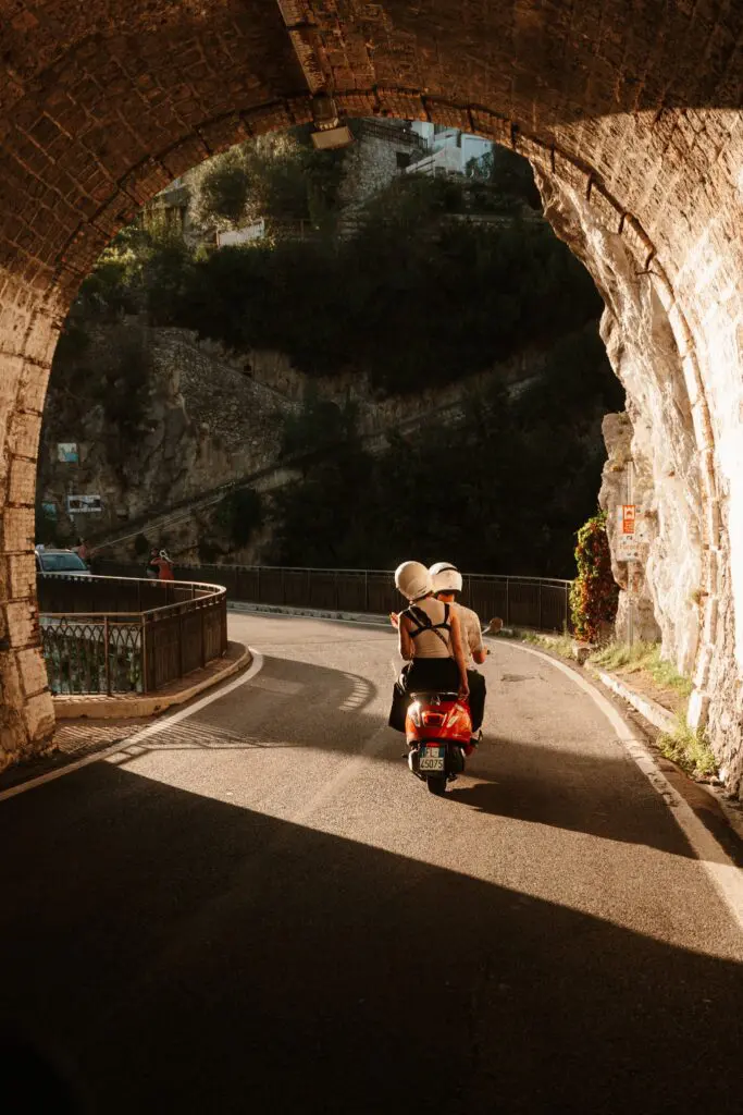 couple on a red scooter driving through an archway in Amalfi