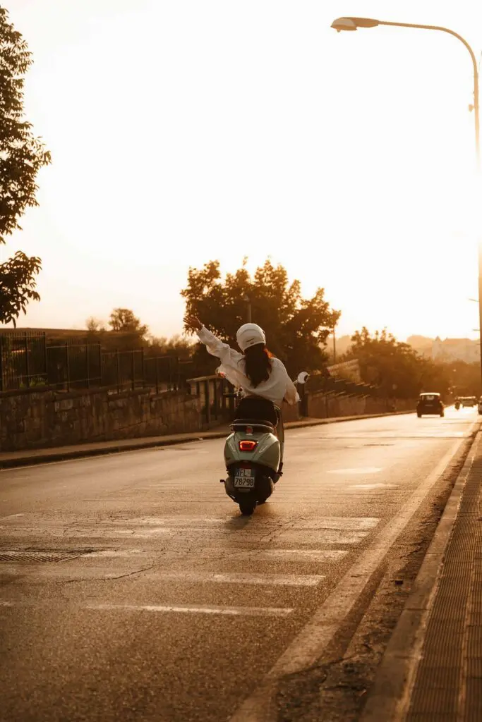 femme sur un scooter, le bras levé, au coucher du soleil à Amalfi
