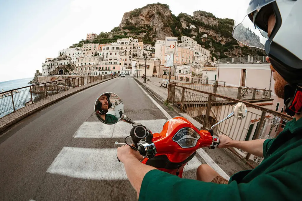 homme sur un scooter Vespa rouge traversant une ville de la côte amalfitaine