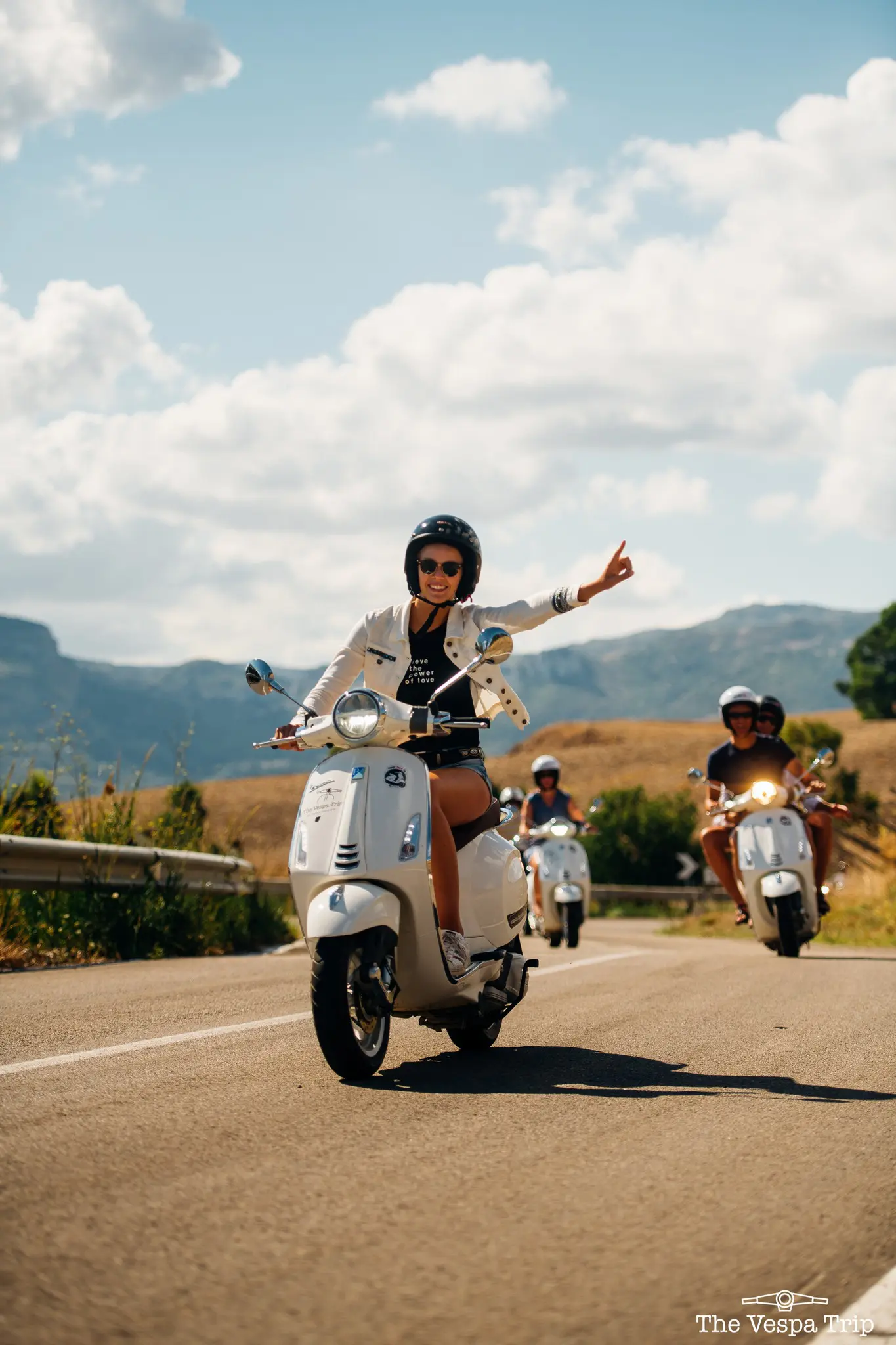 groupe de personnes roulant sur des Vespas blanches sur une route ensoleillée en Sicile