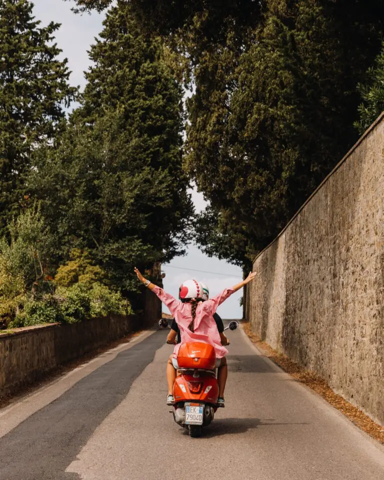 woman on back of scooter with arms out in Tuscany