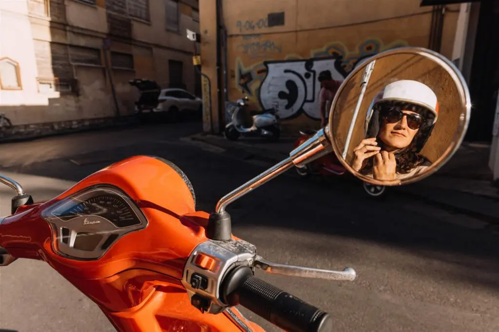 femme casquée reflétée dans le rétroviseur d’un scooter en Toscane