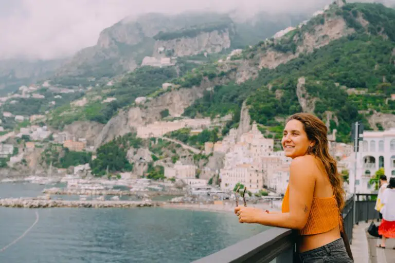femme souriante devant un village de la côte amalfitaine et les montagnes