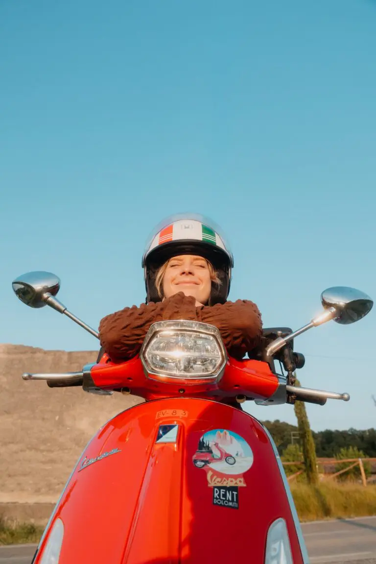 woman in helmet on red Vespa scooter in Venet…