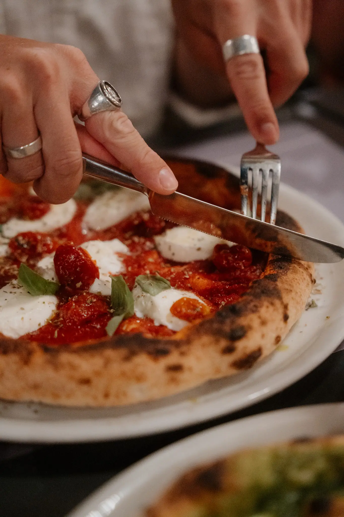 mains découpant une pizza fraîche garnie de mozzarella et de basilic