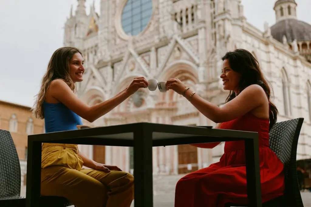 two women toasting espresso in front of Siena Cathedral