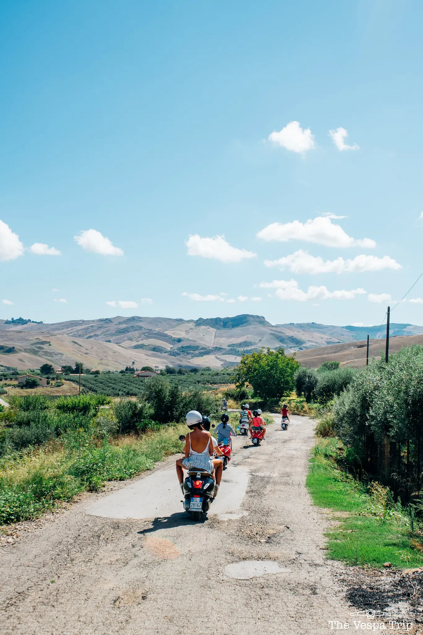 group of people riding vespas on a rural road in Sicily