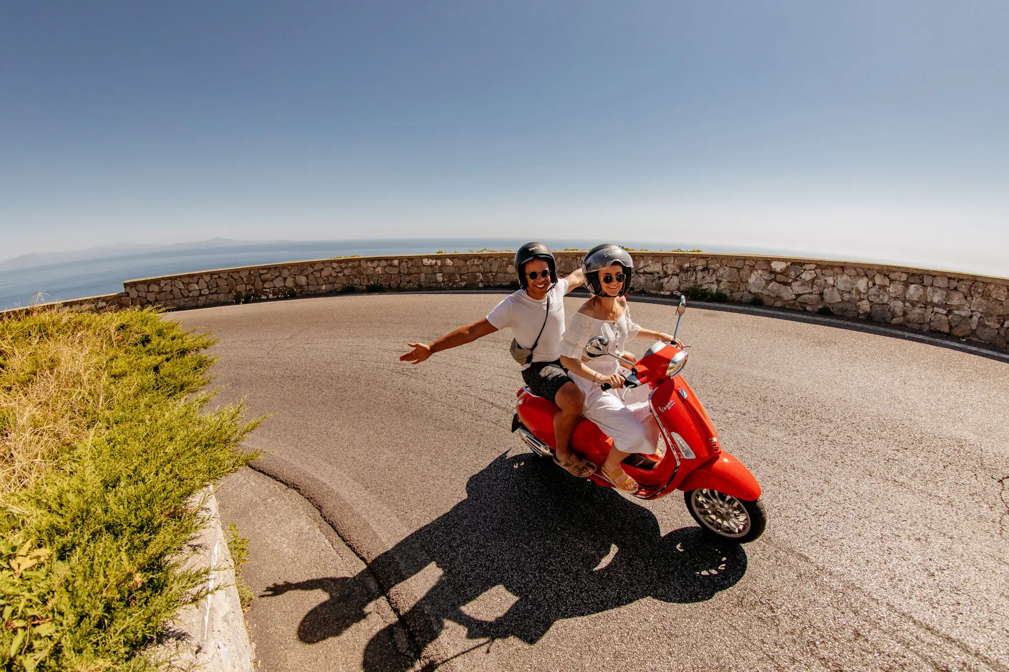 couple roulant sur un scooter Vespa rouge sur une route côtière