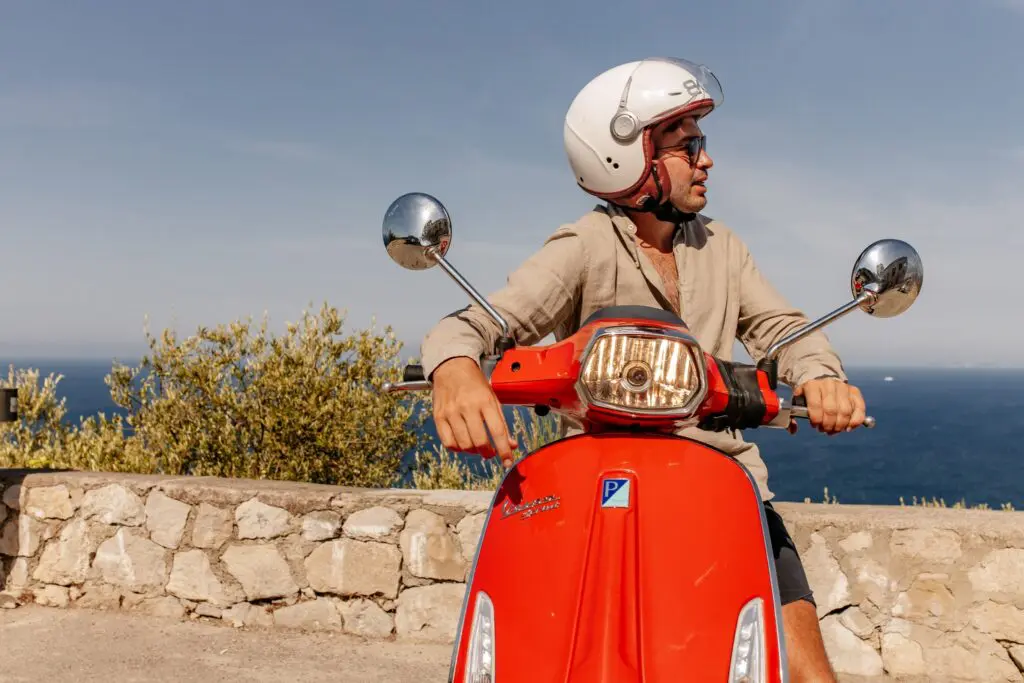 homme sur un scooter Vespa rouge avec vue sur la mer