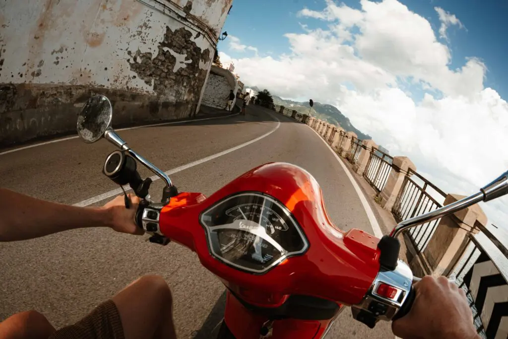 personne conduisant un scooter Vespa rouge sur une route côtière à Amalfi
