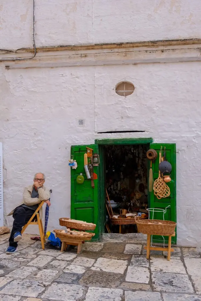 homme assis devant une boutique aux portes vertes à Ostuni, dans les Pouilles