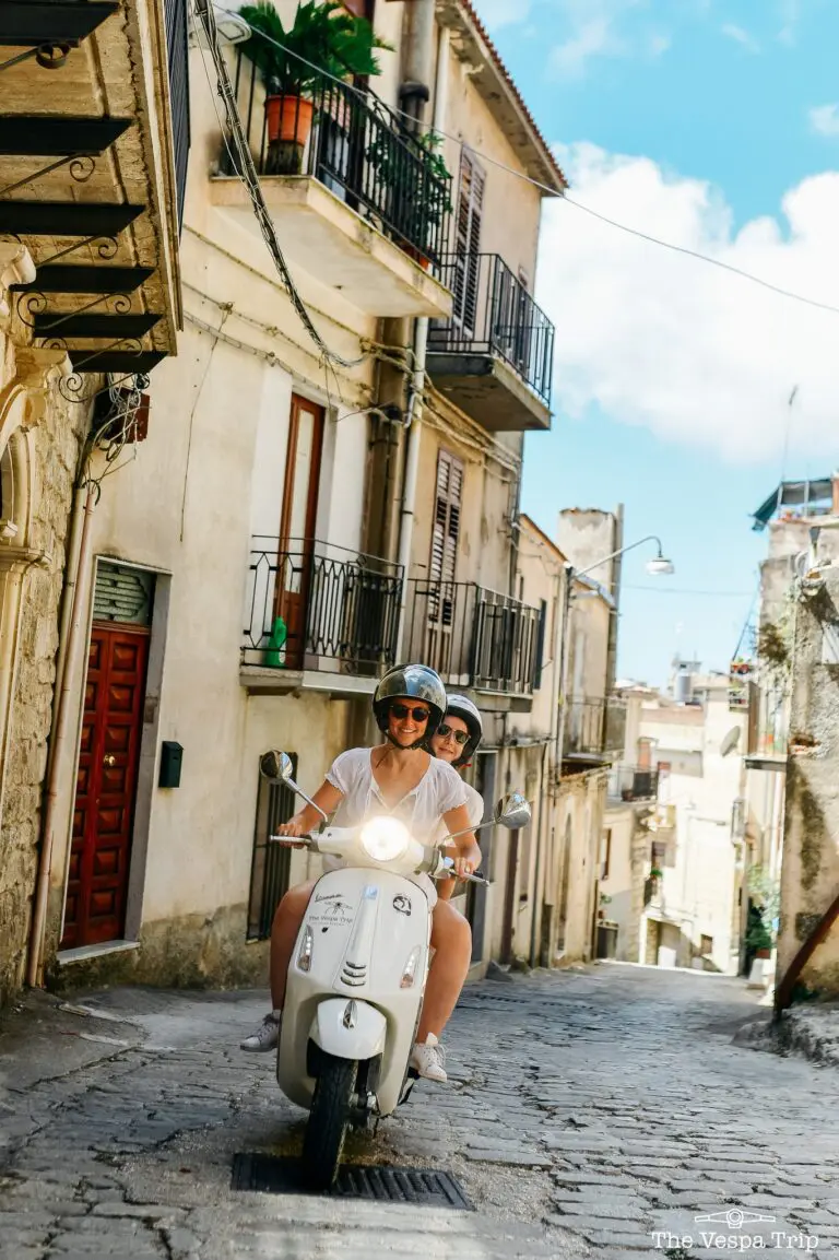 deux femmes à Vespa blanche dans une rue pavée de Sicile