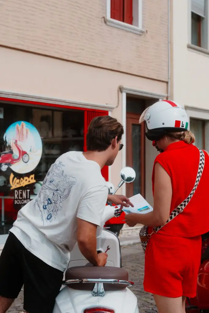 couple regardant une carte à côté d’un scooter Vespa blanc