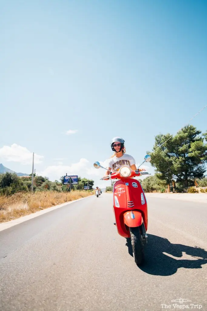 personne conduisant un scooter Vespa rouge sur une route ensoleillée en Sicile