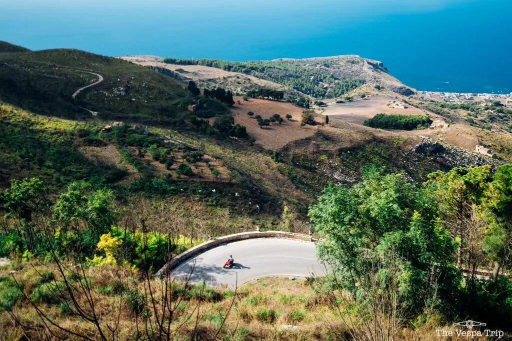 vespa rouge sur une route sinueuse surplombant la mer en Sicile