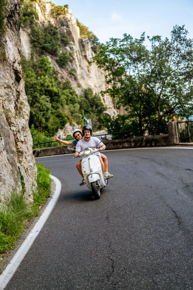 Deux personnes chevauchant une Vespa blanche le long de la côte amalfitaine.