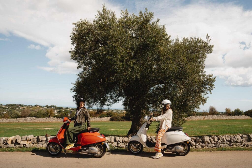 deux femmes sur des vespas devant un olivier