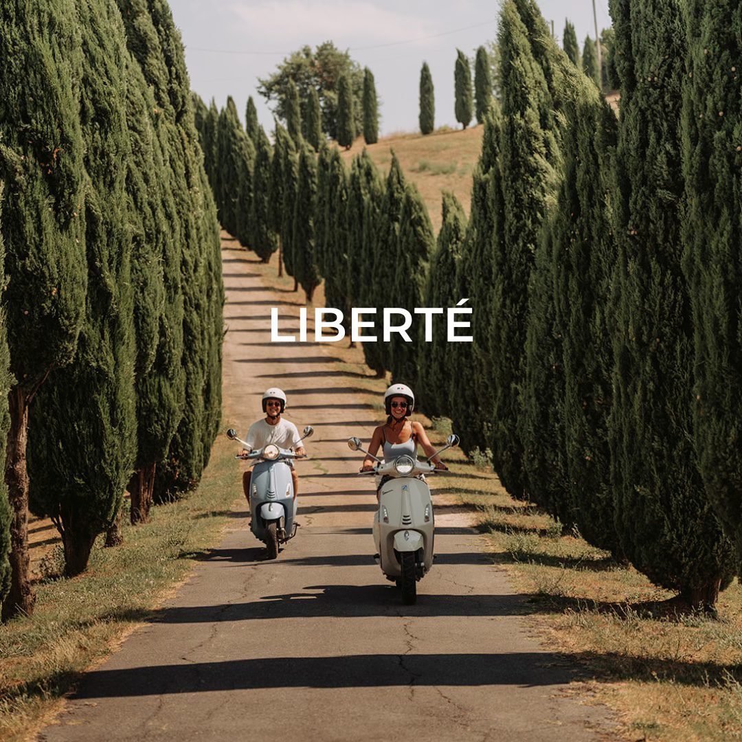 Deux personnes sur une Vespa en Toscane entre les vignobles et les cyprès, deux personnes sur la Vespa traversent un paysage pittoresque en Toscane, entourées de pins parasols.